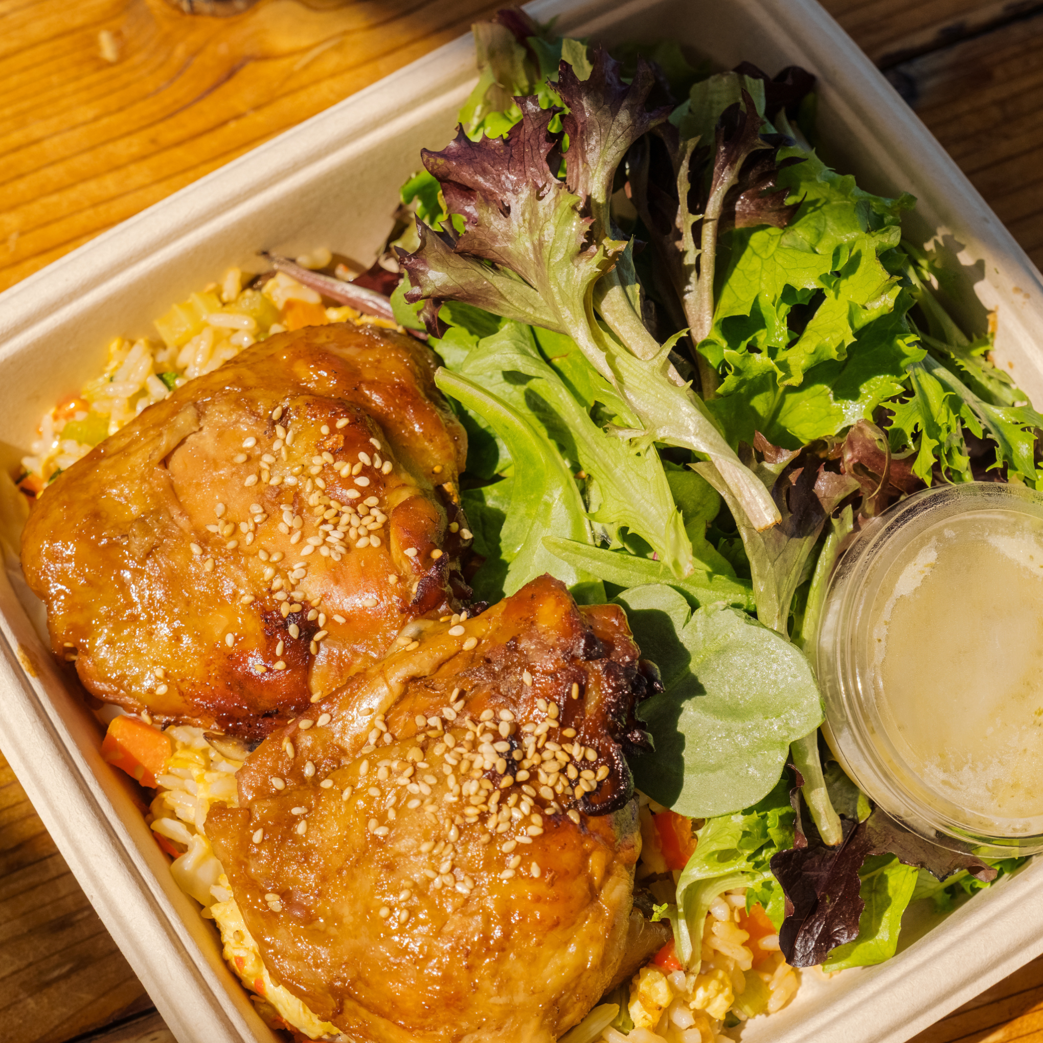 Box with glazed chicken thighs, mixed greens, and dressing.