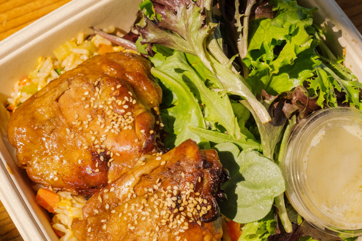 Box with glazed chicken thighs, mixed greens, and dressing.