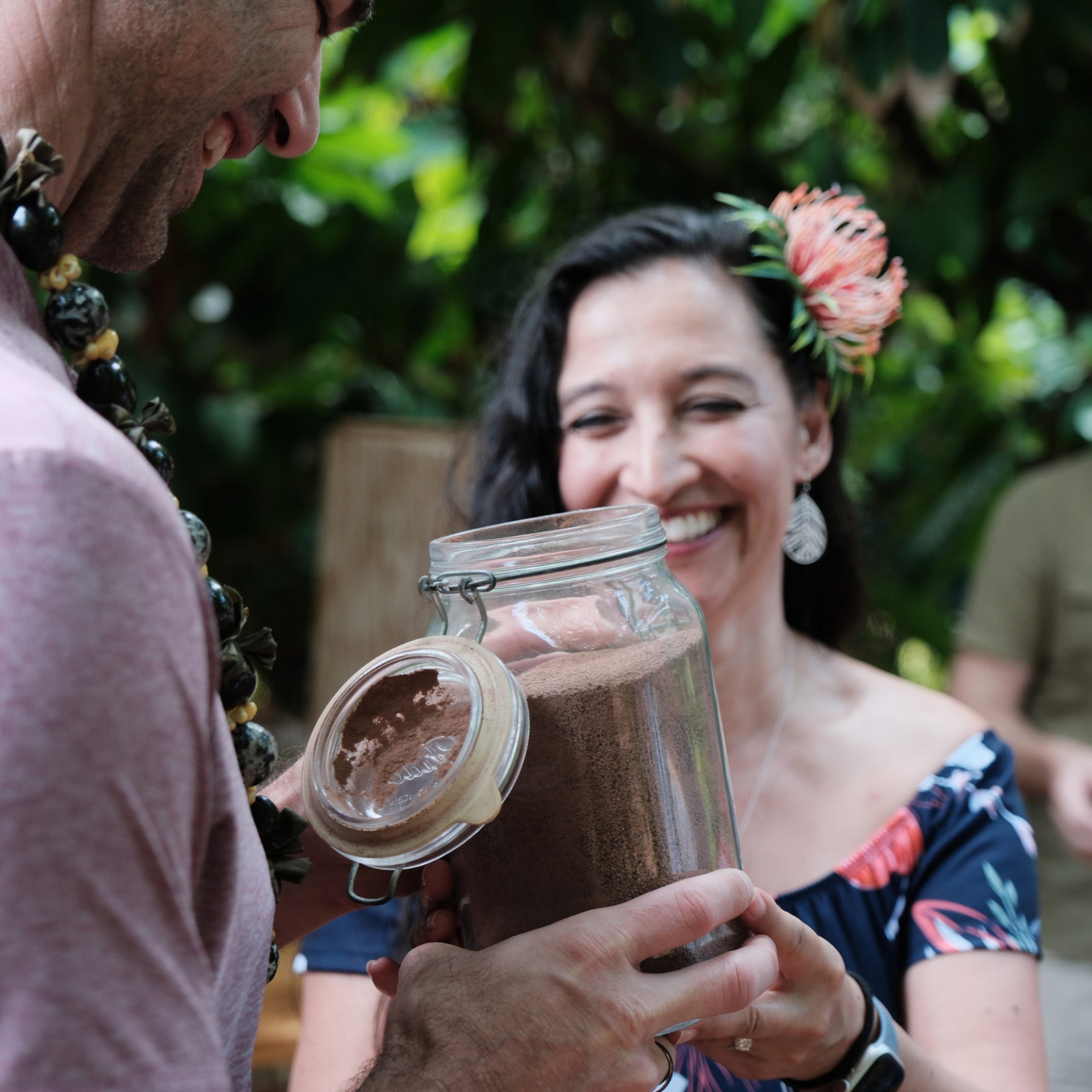 Woman smiles while accepting a jar of brown powder from a man outdoors.