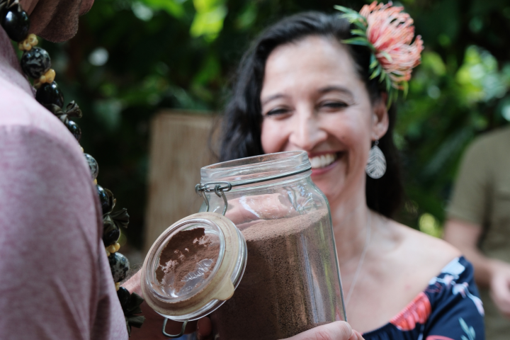 Woman smiles while accepting a jar of brown powder from a man outdoors.