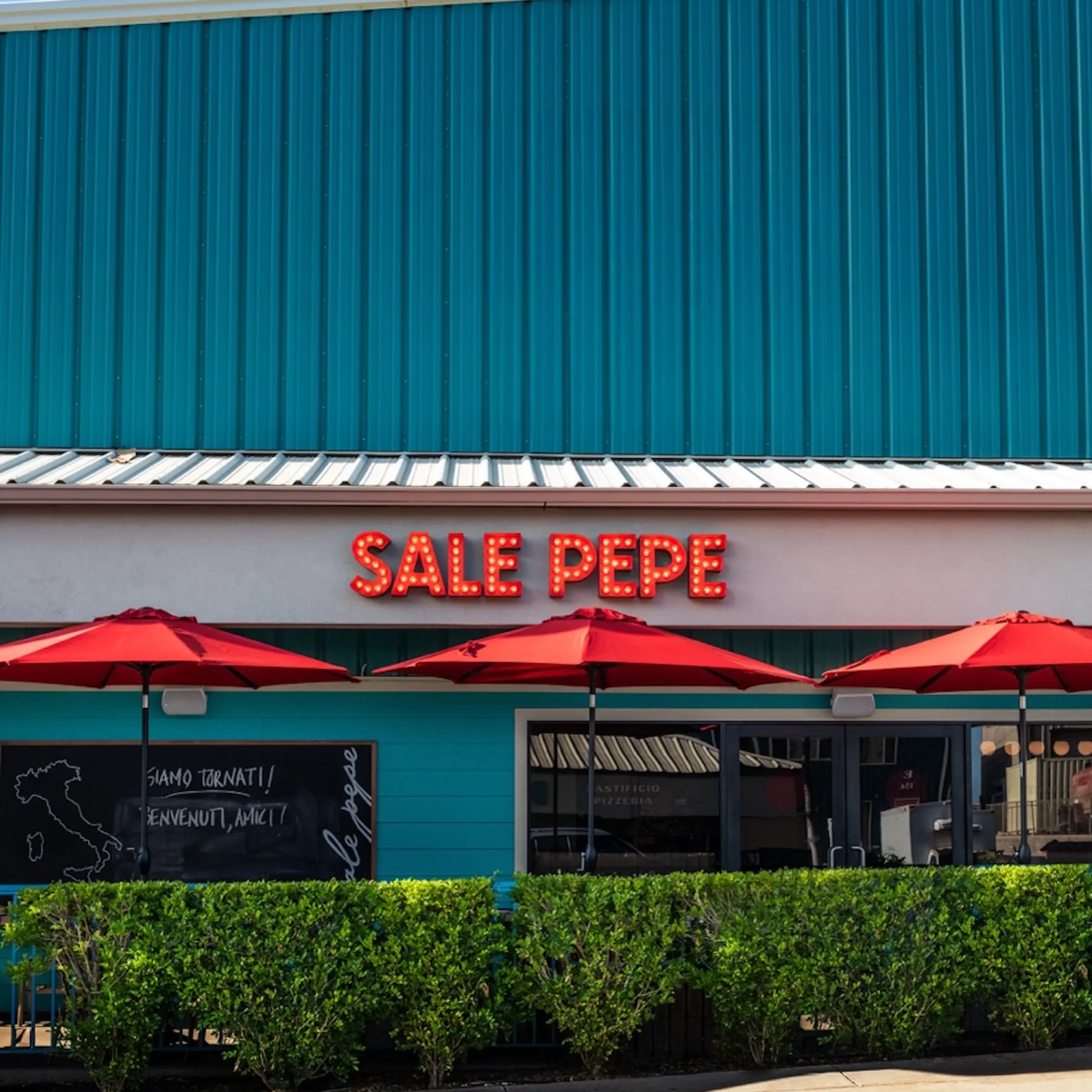 Restaurant facade with teal wall, red umbrellas, and sign reading 'Sale Pepe'.