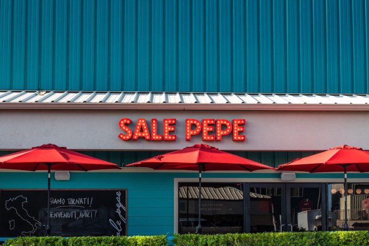 Restaurant facade with teal wall, red umbrellas, and sign reading 'Sale Pepe'.