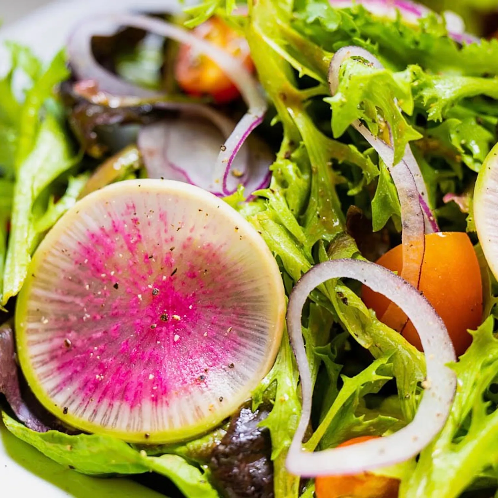 Colorful salad with watermelon radishes, red onion slices, and mixed greens.