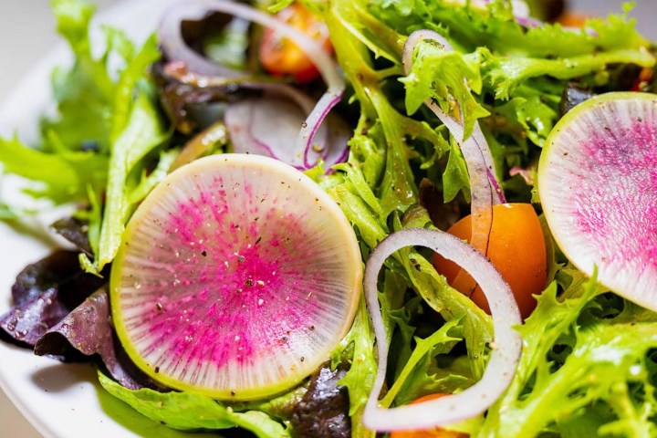 Colorful salad with watermelon radishes, red onion slices, and mixed greens.