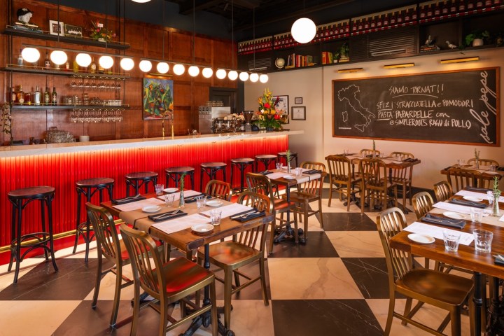 Cozy Italian restaurant interior with red-lit bar, wooden tables, and chalkboard menu.