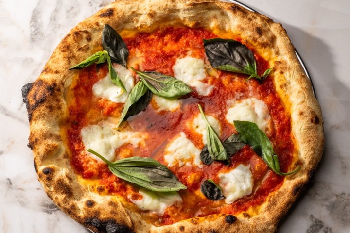 Pizza with tomato sauce, mozzarella, and basil on a marble surface.