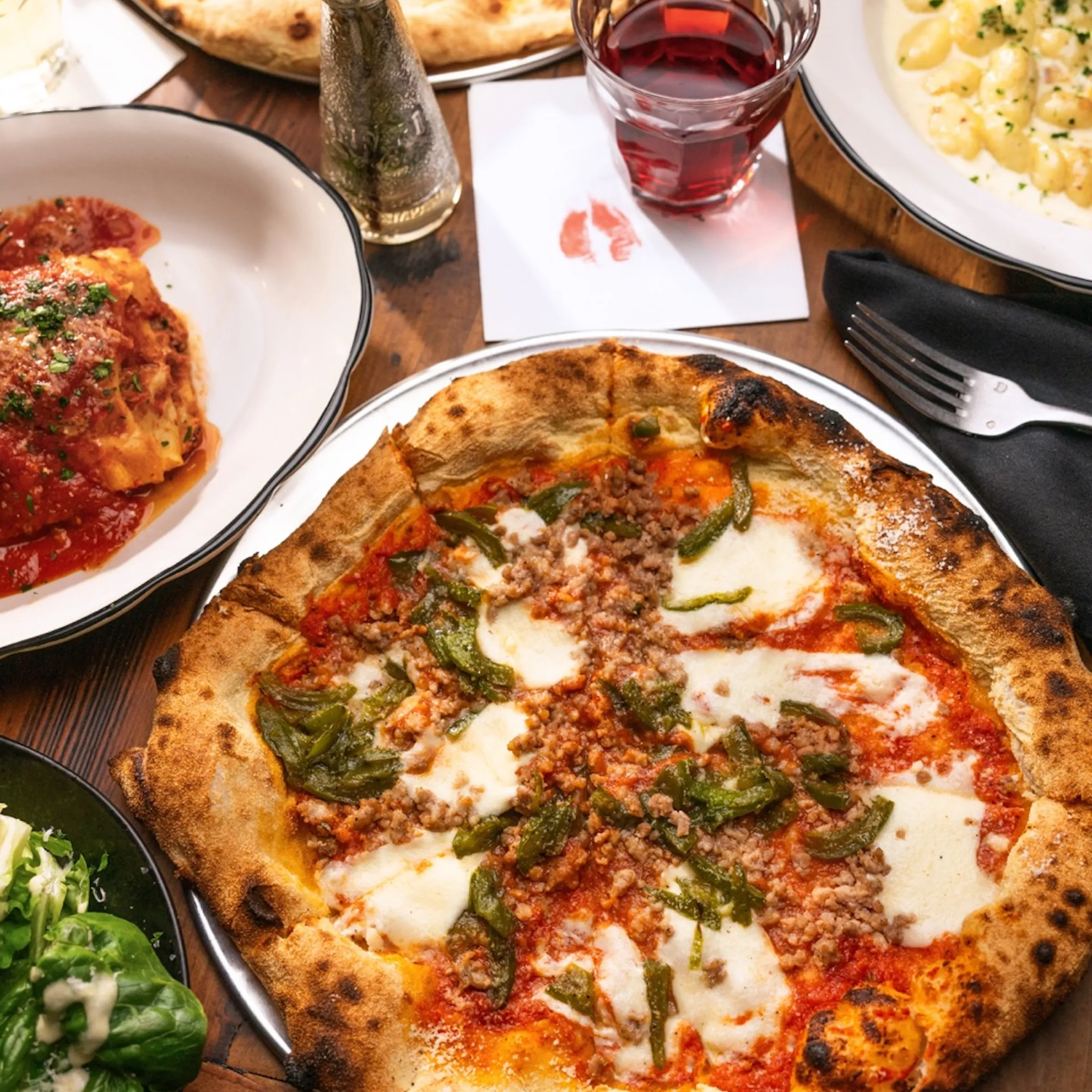 Pizza, pasta, and salad on a wooden table with a glass of red wine.
