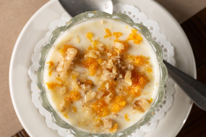 Glass bowl of yogurt with orange zest and walnuts on a plate with a spoon.