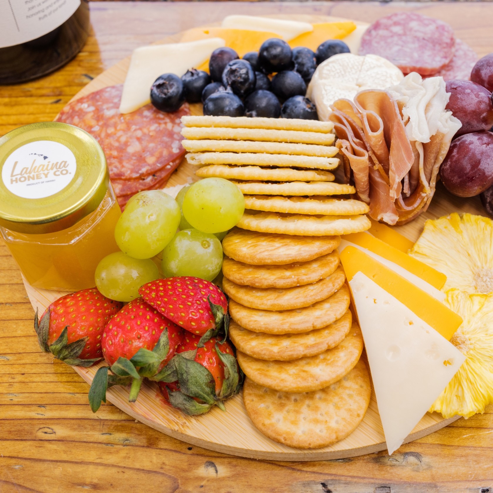 Charcuterie board with cheeses, crackers, fruits, and meats on a wooden table.