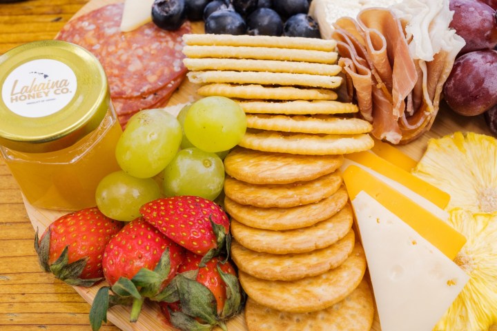 Charcuterie board with cheeses, crackers, fruits, and meats on a wooden table.