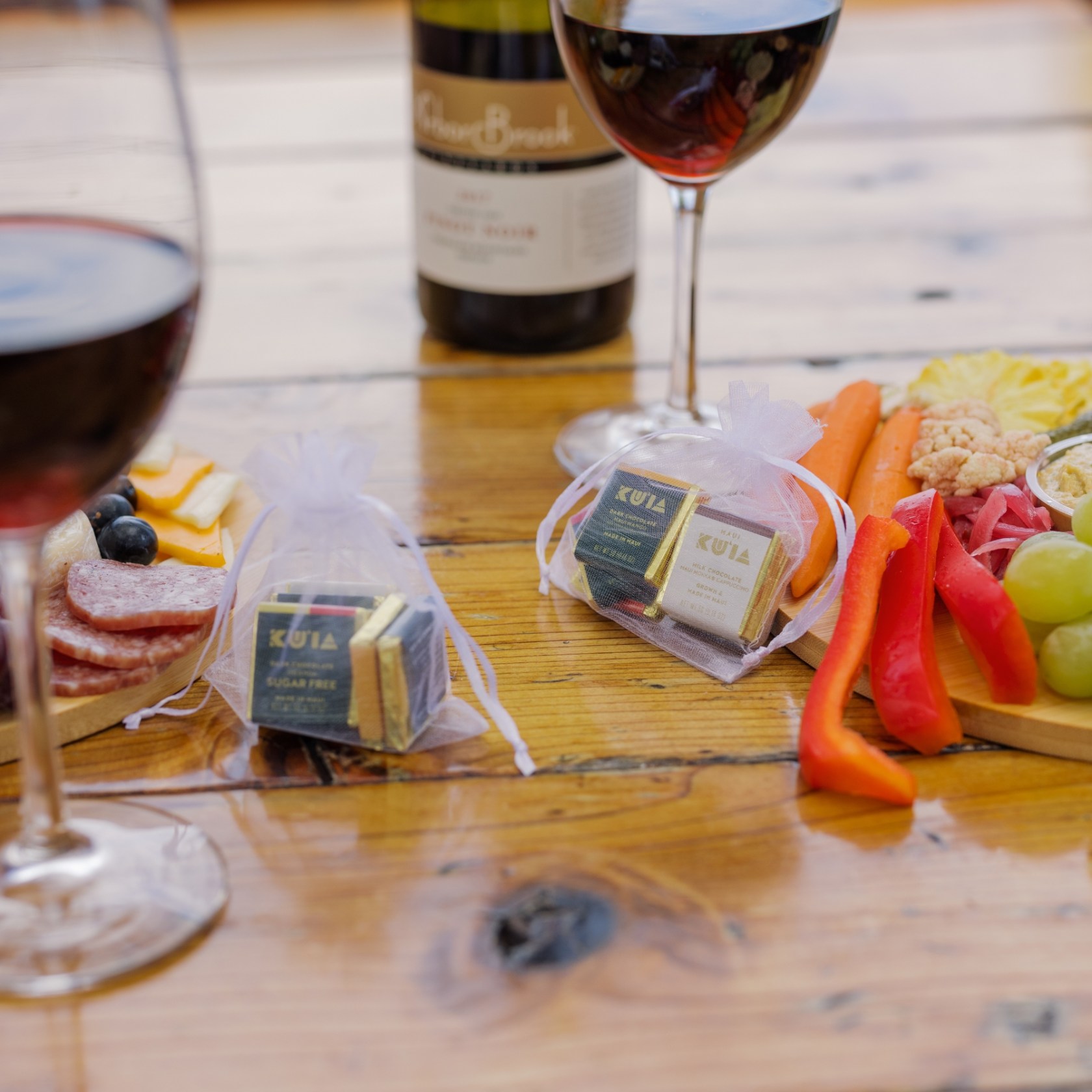 Wine glasses, cheese, meats, fruits, and chocolates on a wooden table.