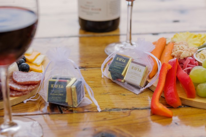 Wine glasses, cheese, meats, fruits, and chocolates on a wooden table.