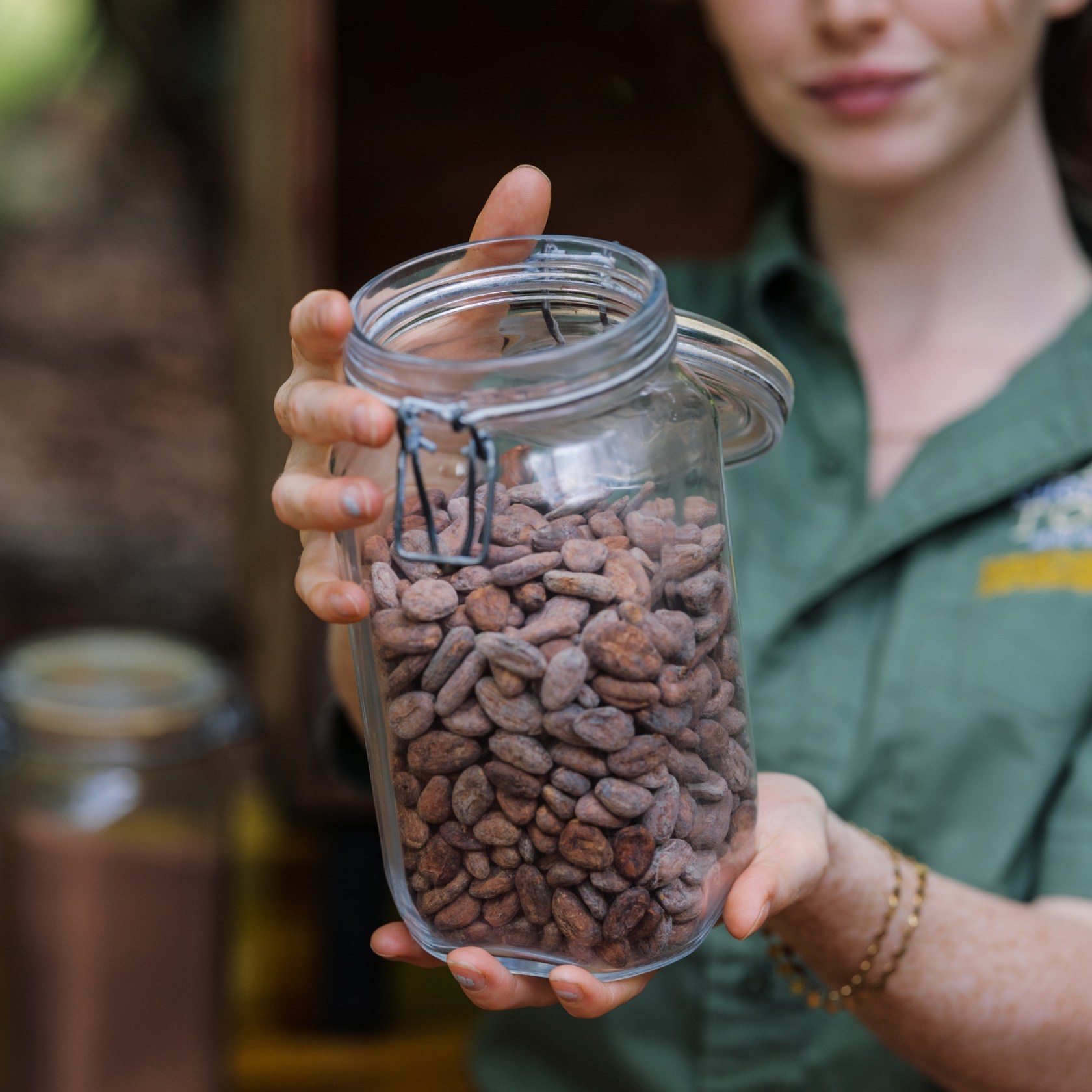 Person holding a jar of cocoa beans outdoors.